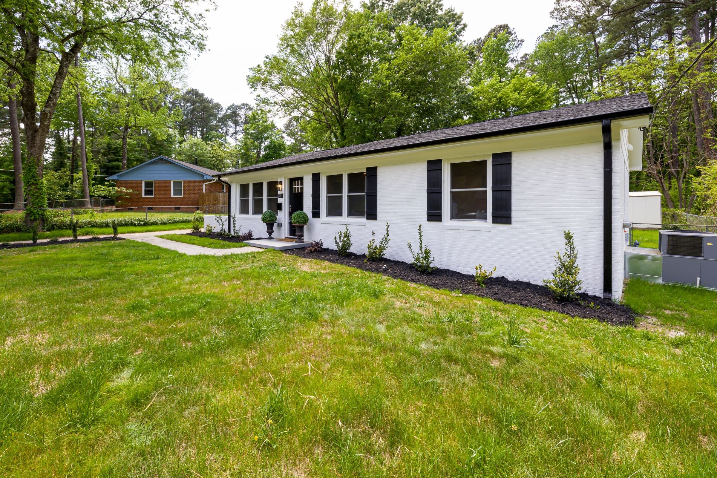 Painted brick ranch house with a wide green lawn and trees