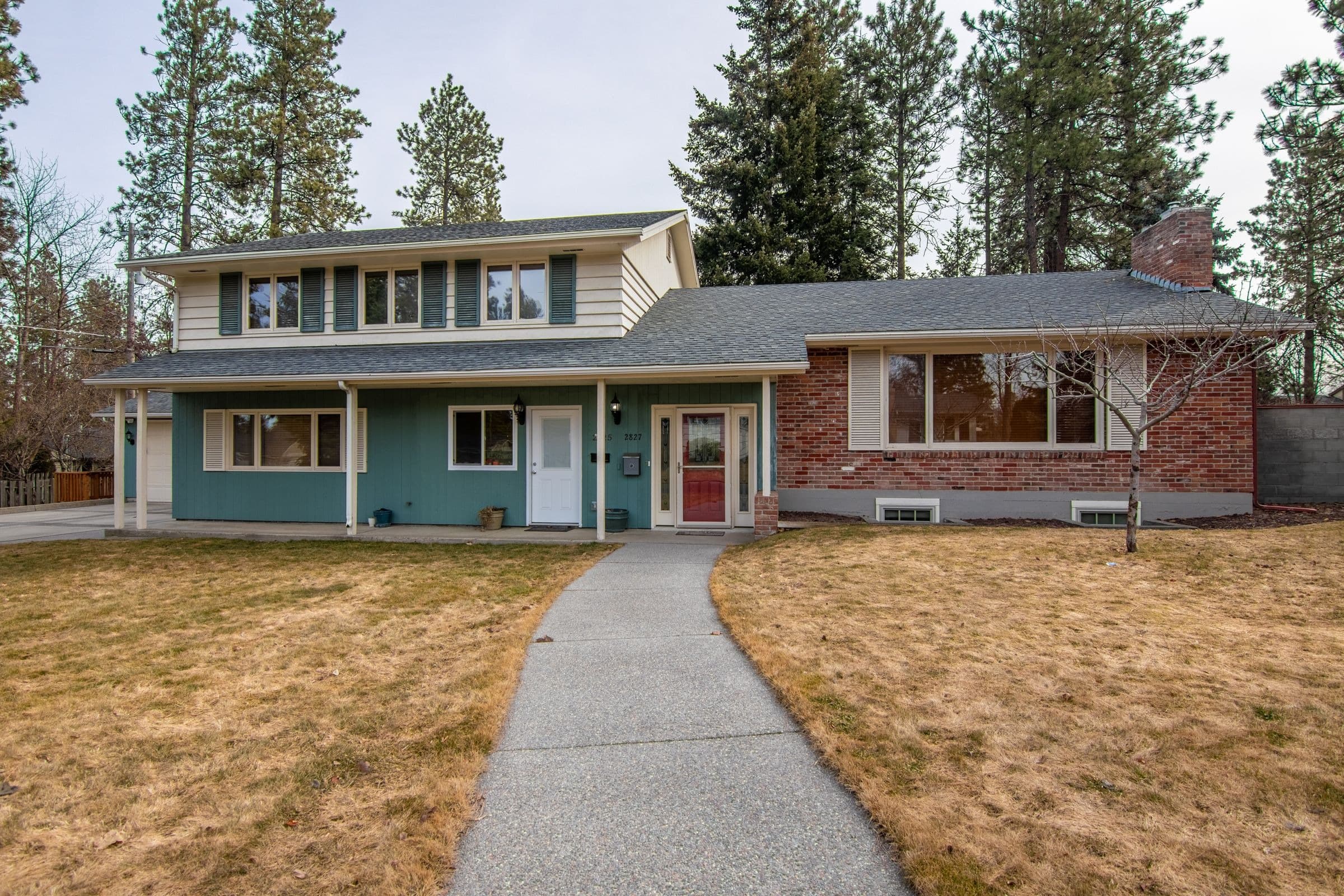 Split-level brick and siding house with a front walk and tall pines